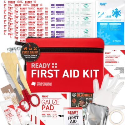 Comprehensive travel first aid kit with a red zippered pouch labeled "Ready First Aid Kit" surrounded by medical supplies including bandages, gauze pads, scissors, gloves, antiseptic wipes, a thermal blanket, and wooden tongue depressors. Designed for emergencies on the go or outdoor travel.