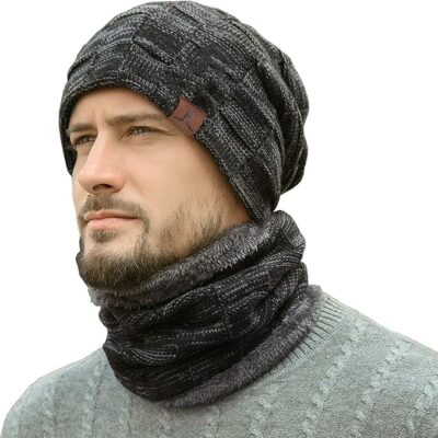 Man wearing a matching dark gray knit hat and scarf set with a textured pattern and leather logo patch on the beanie. The cozy, winter-ready set pairs a slouchy beanie with a thick neck warmer, ideal for cold weather.