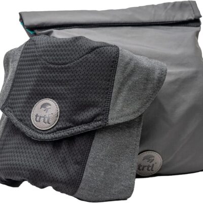Gray Trtl travel pillow with a soft, ergonomic wrap design shown folded next to its matching compact carrying pouch. The pillow features a supportive internal structure for neck comfort during travel and is branded with the Trtl logo.